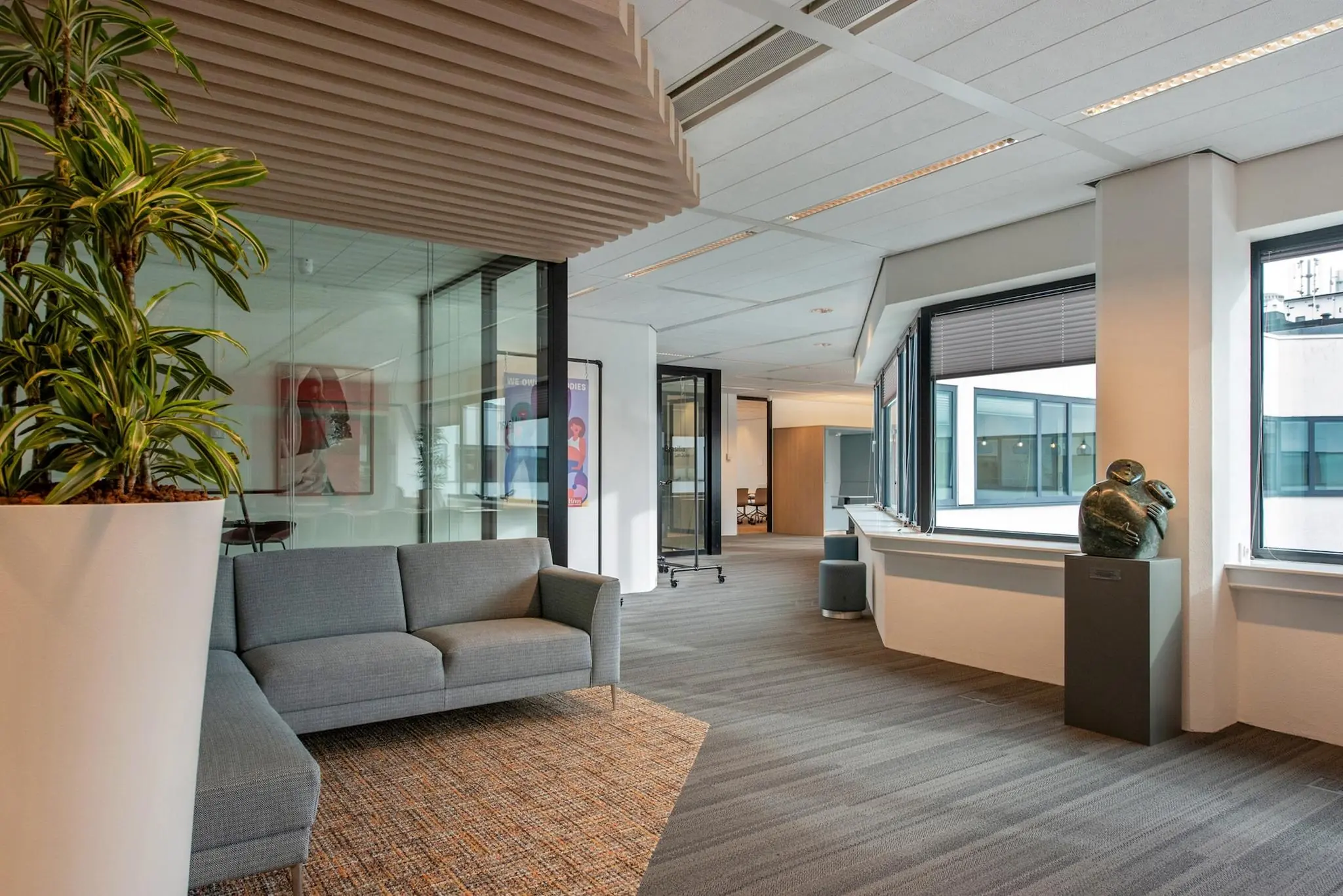 Moderne kantoorruimte aan de Grote Marktstraat met grijze zithoek, kunstwerken en grote ramen met uitzicht op het tegenoverliggende gebouw.